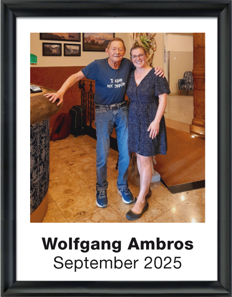 Wolfgang Ambros und eine Frau posieren in einem Raum mit braunem Boden und dunklen Wandgemälden, September 2025.