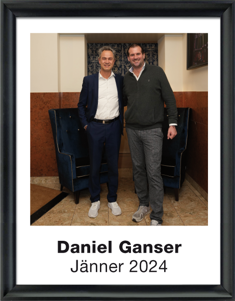 Zwei Männer in legerer Kleidung stehen nebeneinander in einem Raum mit blauen Sesseln im Hintergrund.