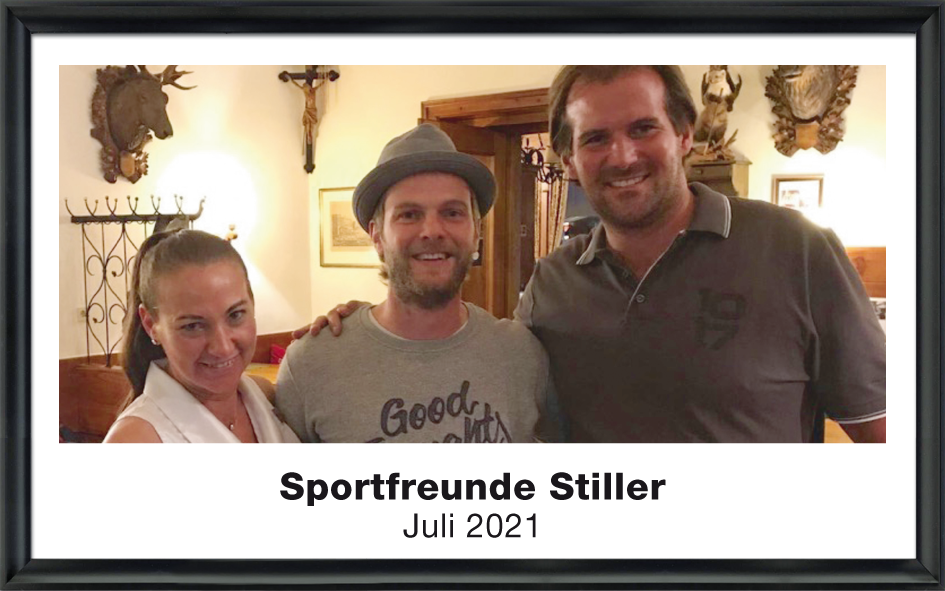 Drei Personen, eine Frau und zwei Männer, lächeln zusammen in einem gemütlichen Raum mit traditioneller Dekoration.