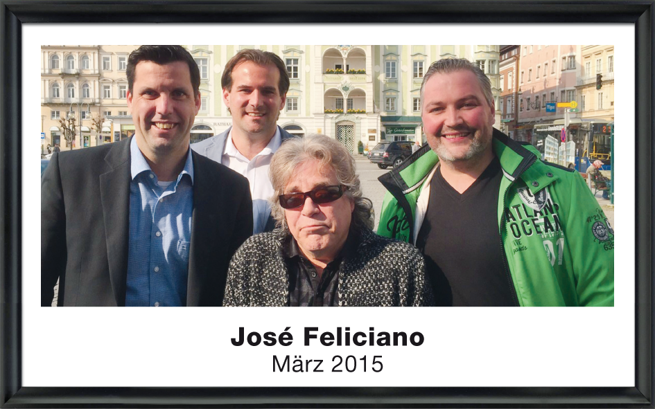José Feliciano mit drei Männern, die auf einem sonnigen Stadtplatz im Hintergrund stehen, März 2015.
