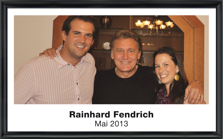 Drei lächelnde Personen posieren eng umarmt vor einem Holzmöbel im Raum.