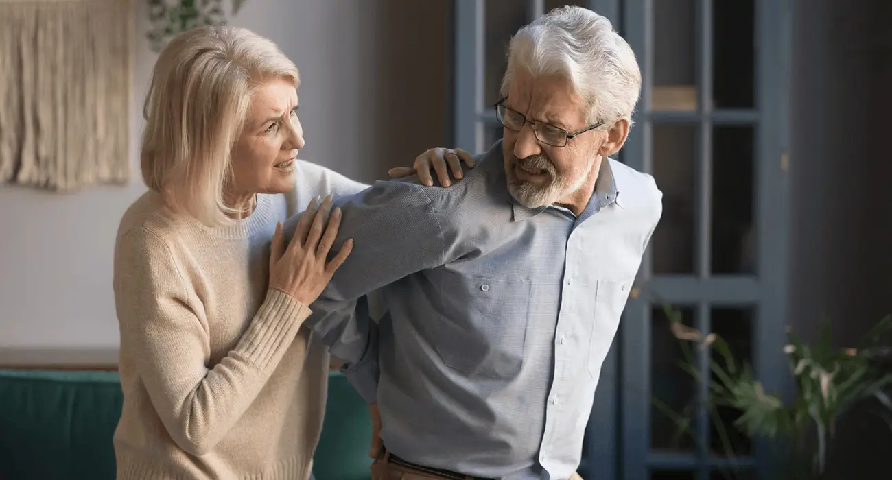 Older man experiencing lumbar back pain and possible spinal stenosis while being supported at home, seeking care from the best spine surgeon in Los Angeles, CA.