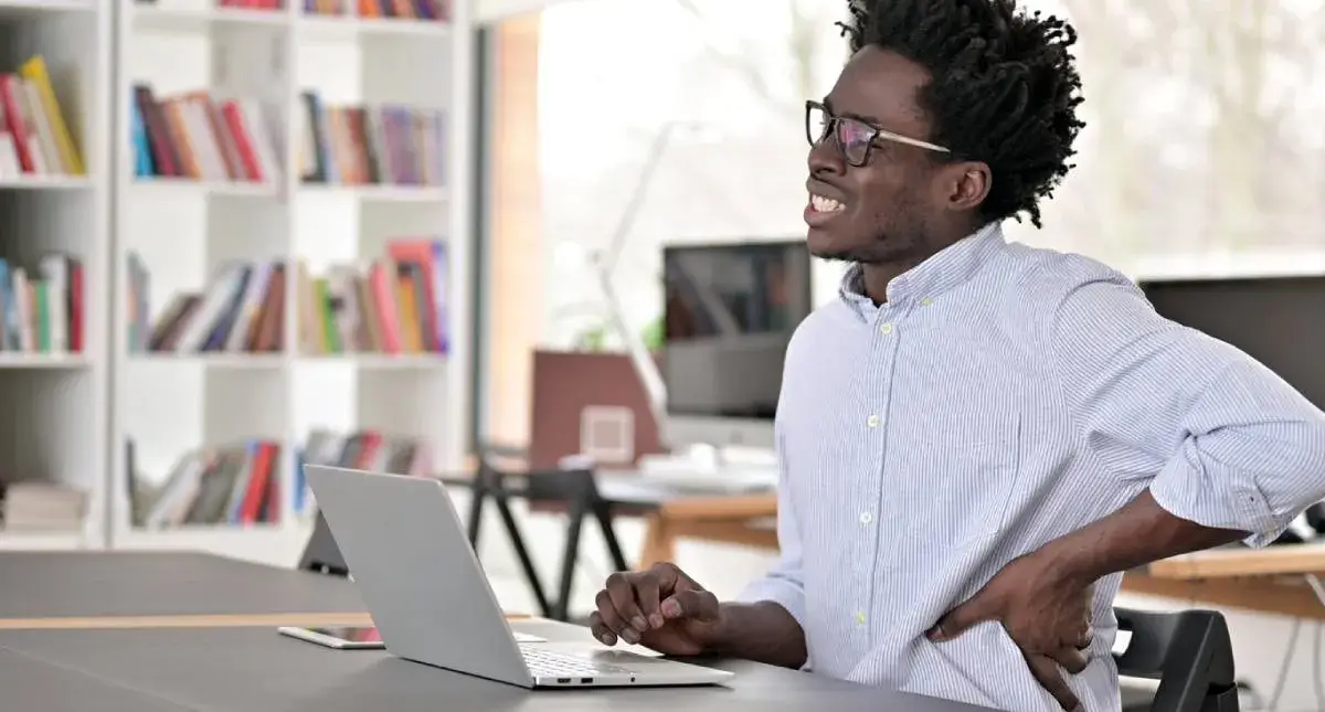 Adult sitting at a desk holding their lower back in pain
