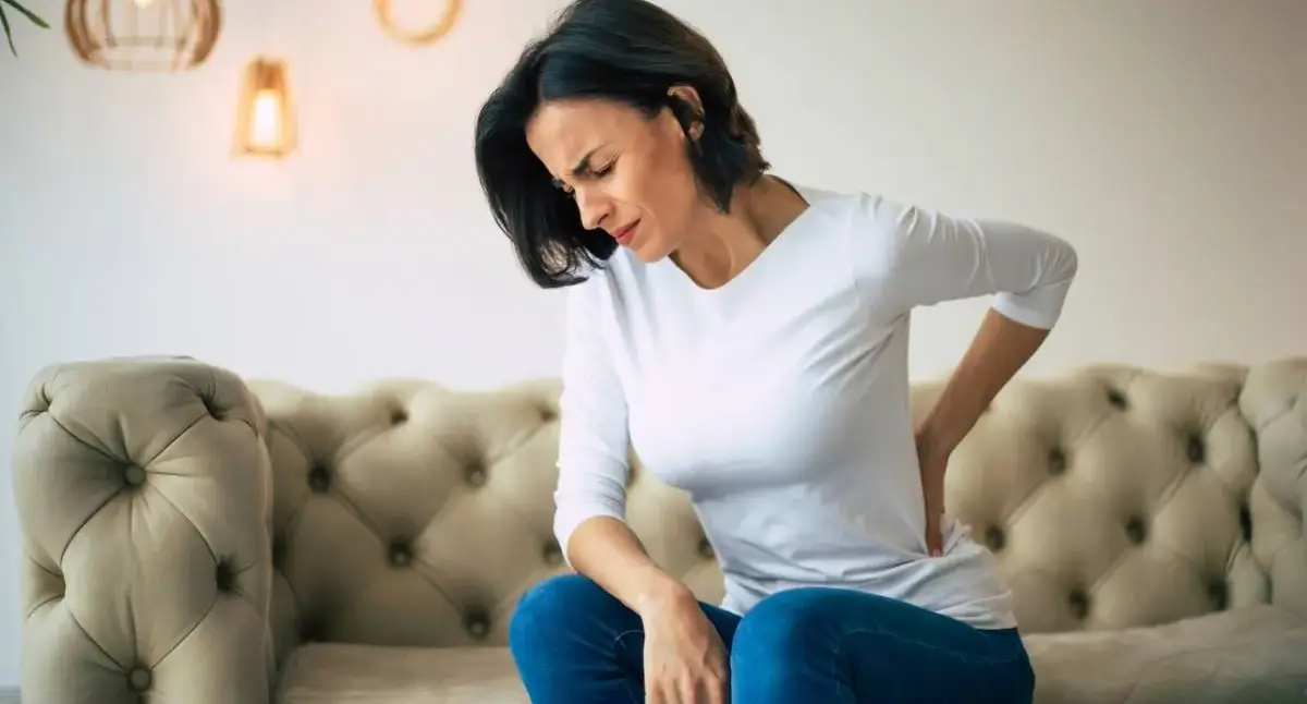 Person holding their lower back in pain while standing at home