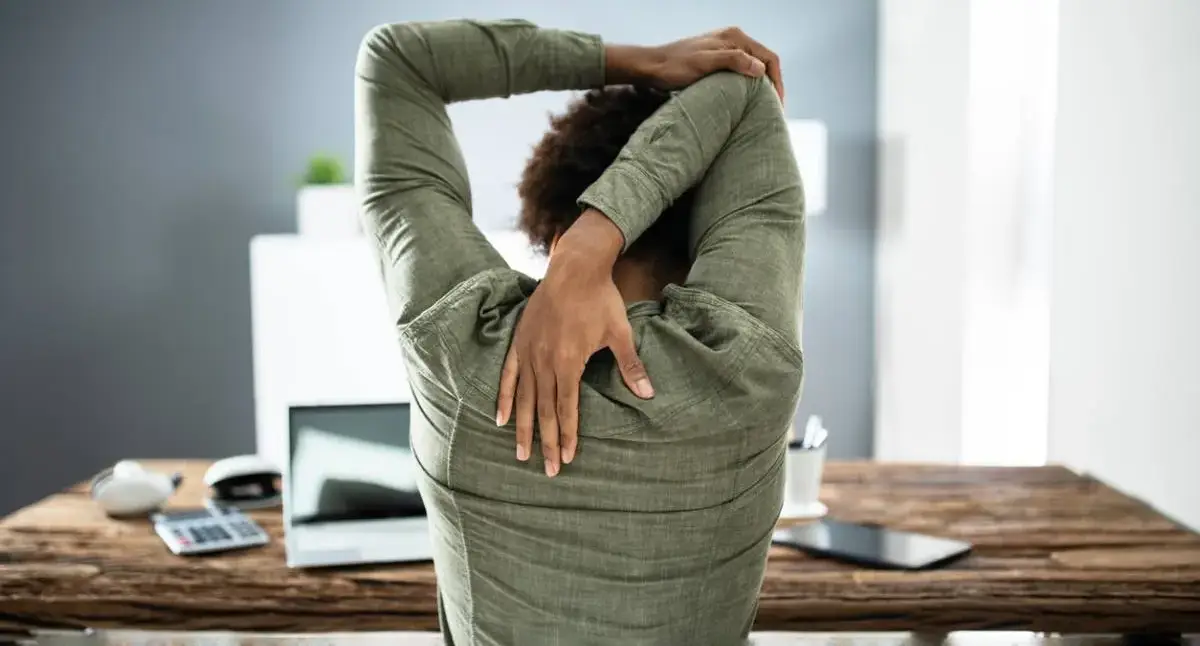 Office worker standing and stretching their lower back next to a desk after prolonged sitting