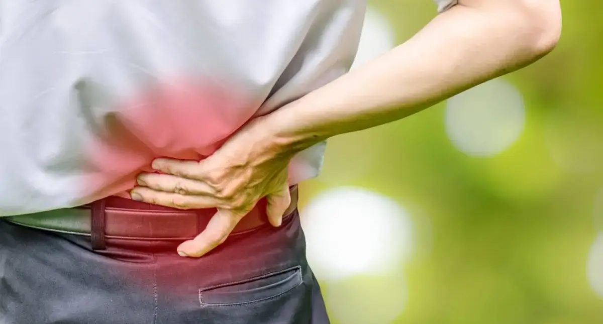 Person holding their lower back while sitting, a common symptom of a spinal disc problem