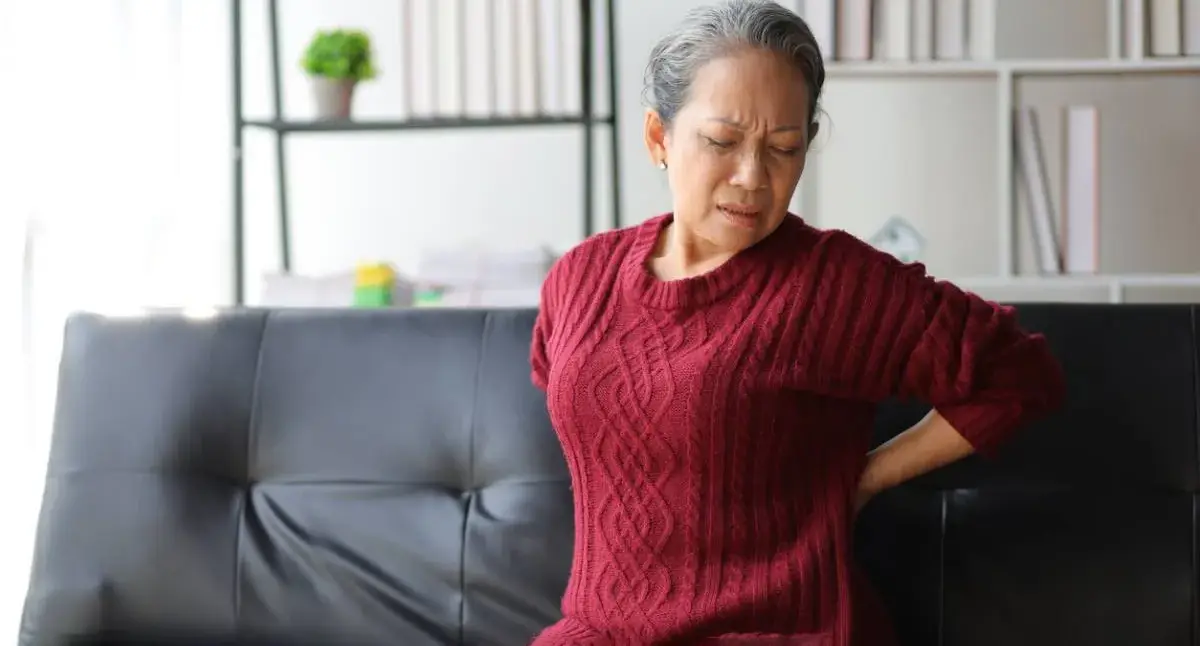 Adult holding their lower back with stiffness consistent with early osteoarthritis symptoms
