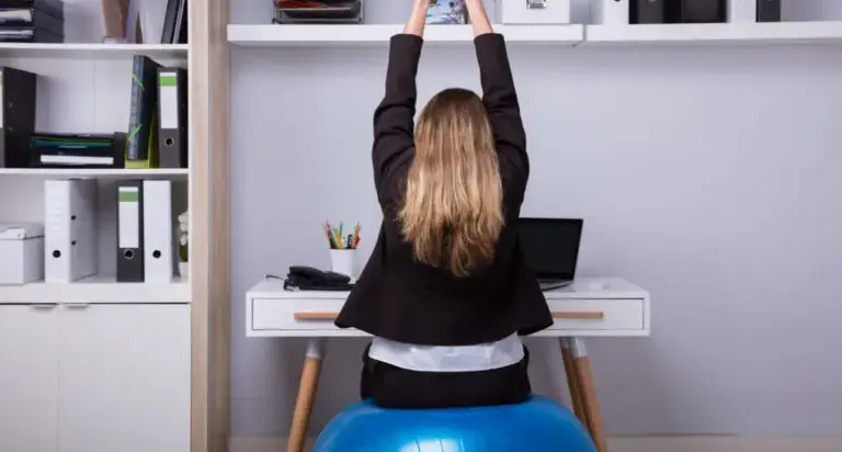 Office worker adjusting chair height and monitor position to reduce neck and low back strain