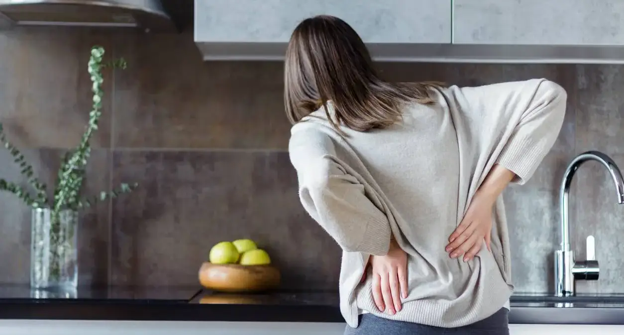 Person stretching their lower back after working at a desk, representing habits that can lead to back pain