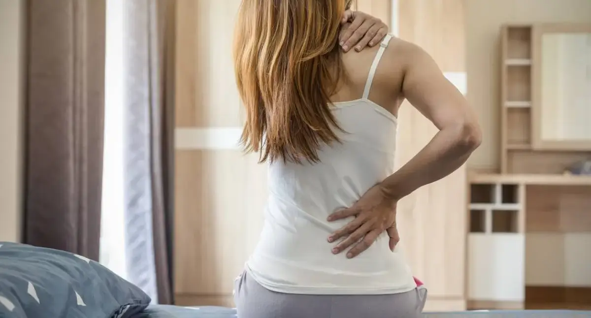 Person holding their lower back while sitting at a desk, illustrating how daily habits can contribute to back pain