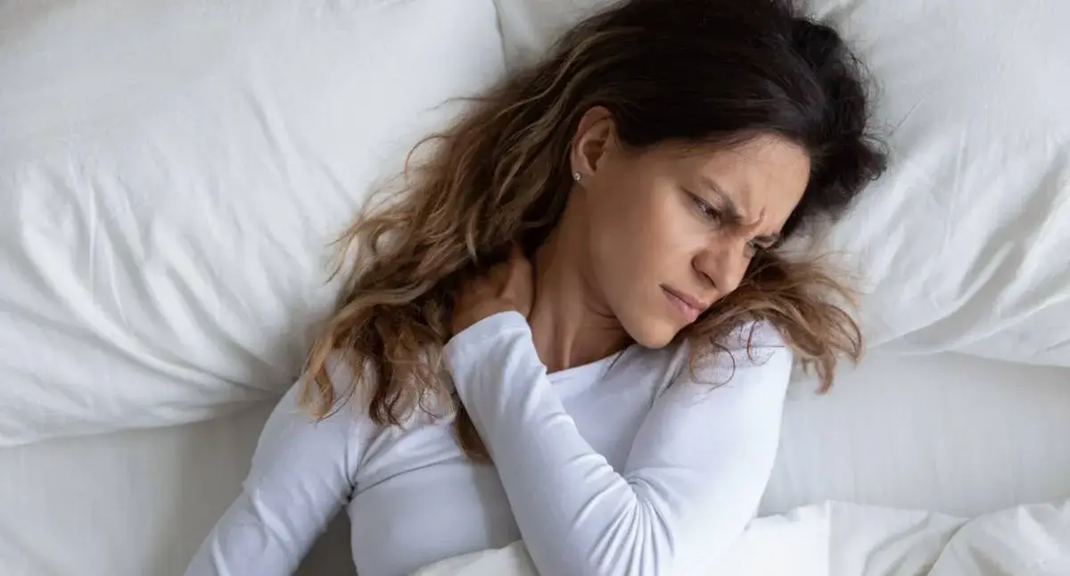 Person adjusting pillows in bed to support the neck and lower back and maintain neutral spinal alignment