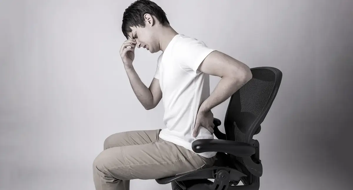 Person holding their lower back in pain while bending forward, illustrating movements that can aggravate a herniated disc
