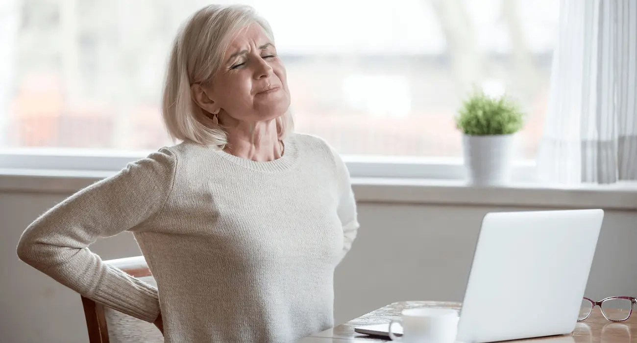 Woman seated at a table holding her lower back, illustrating persistent disc-related back pain that may be evaluated for