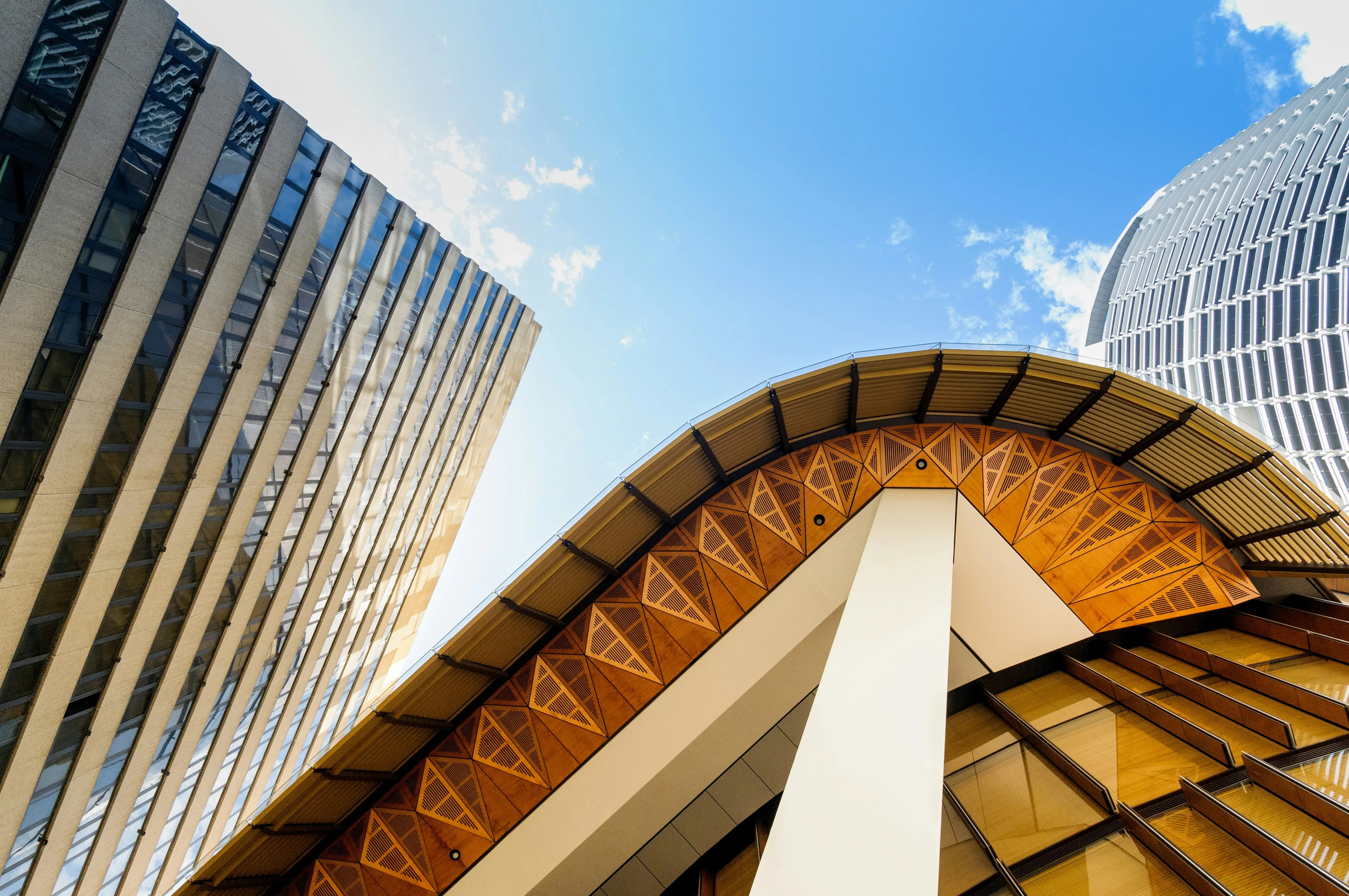 View of modern skyscrapers and a building with a wooden patterned overhang against a blue sky.