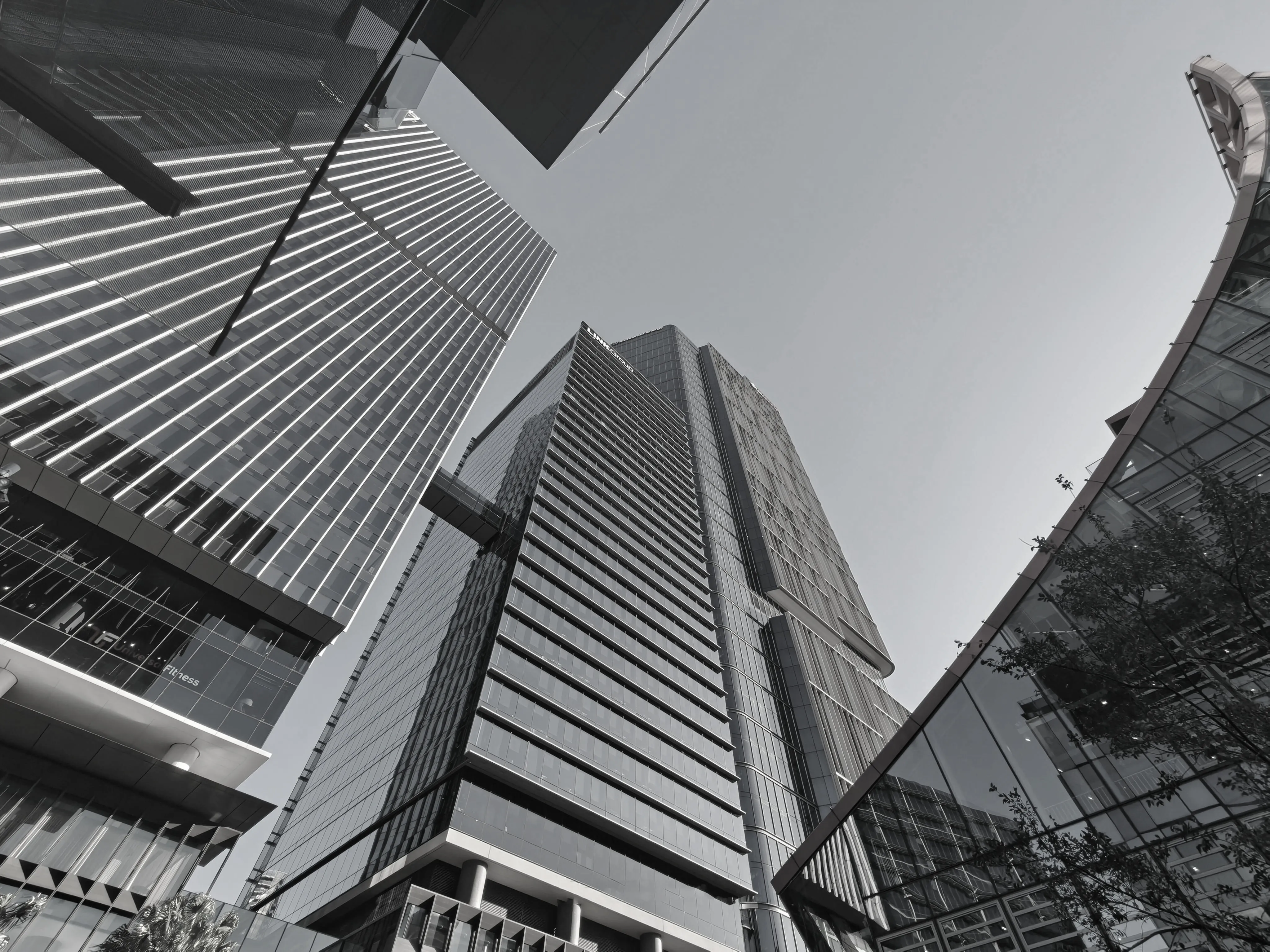 Low-angle black and white photo of modern skyscrapers with glass facades and a skybridge.