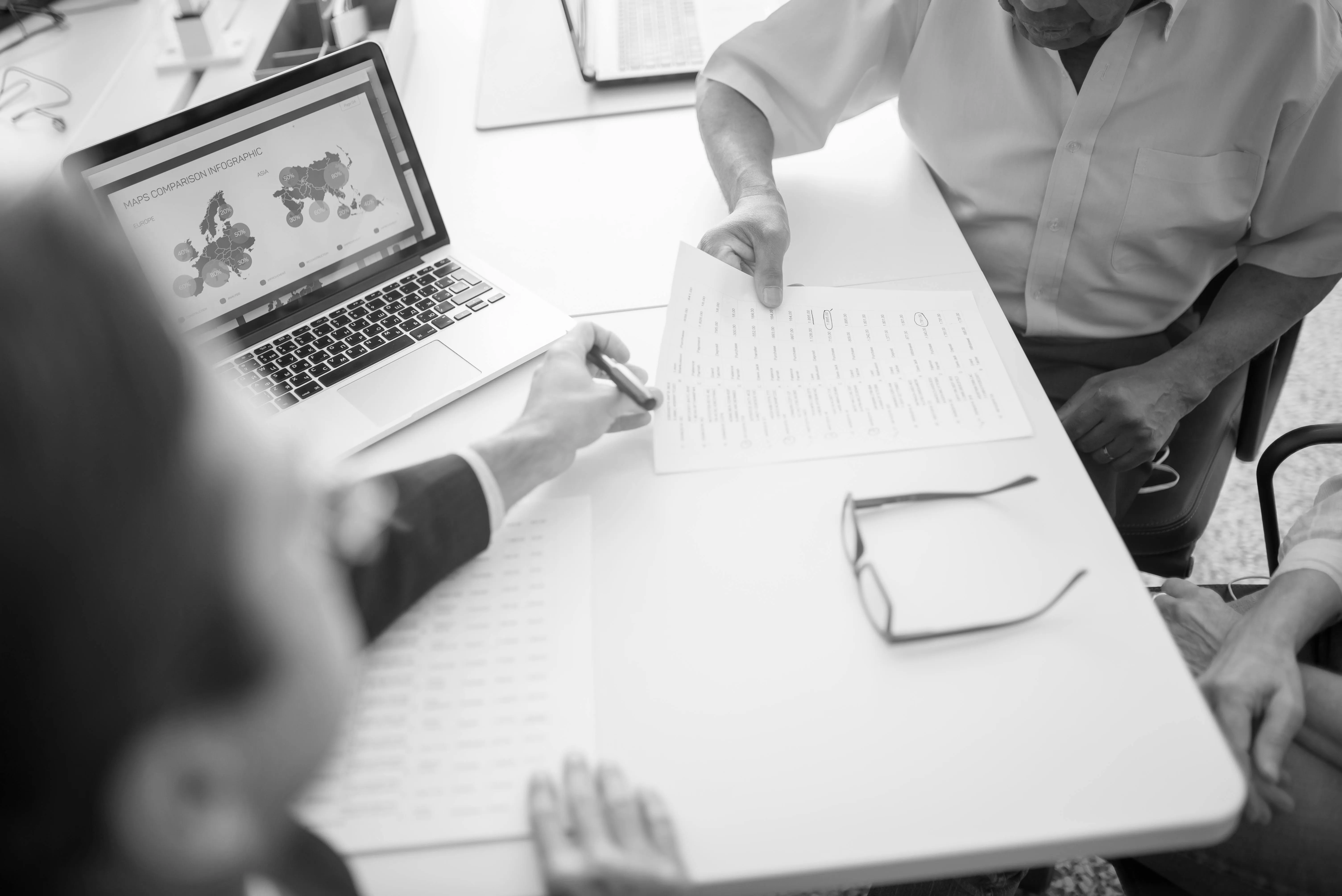 Two people reviewing a printed document at a desk with a laptop showing a maps comparison infographic.