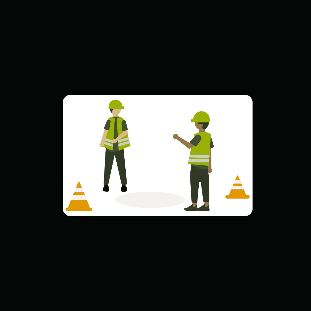 Two construction workers wearing green safety vests and helmets standing near orange traffic cones.