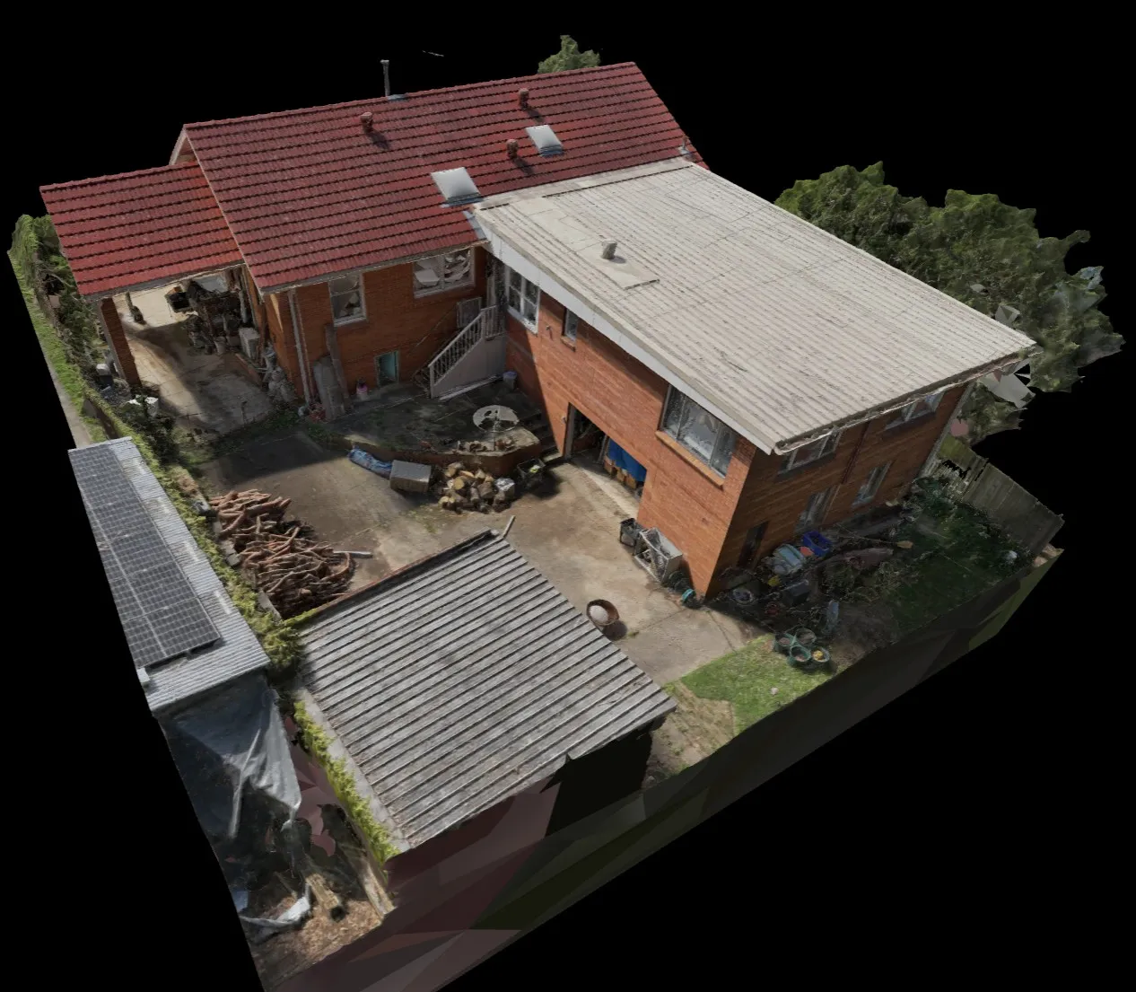 Aerial view of a two-story brick house with red tiled and white flat roofs, a driveway with stacked firewood, and surrounding greenery.