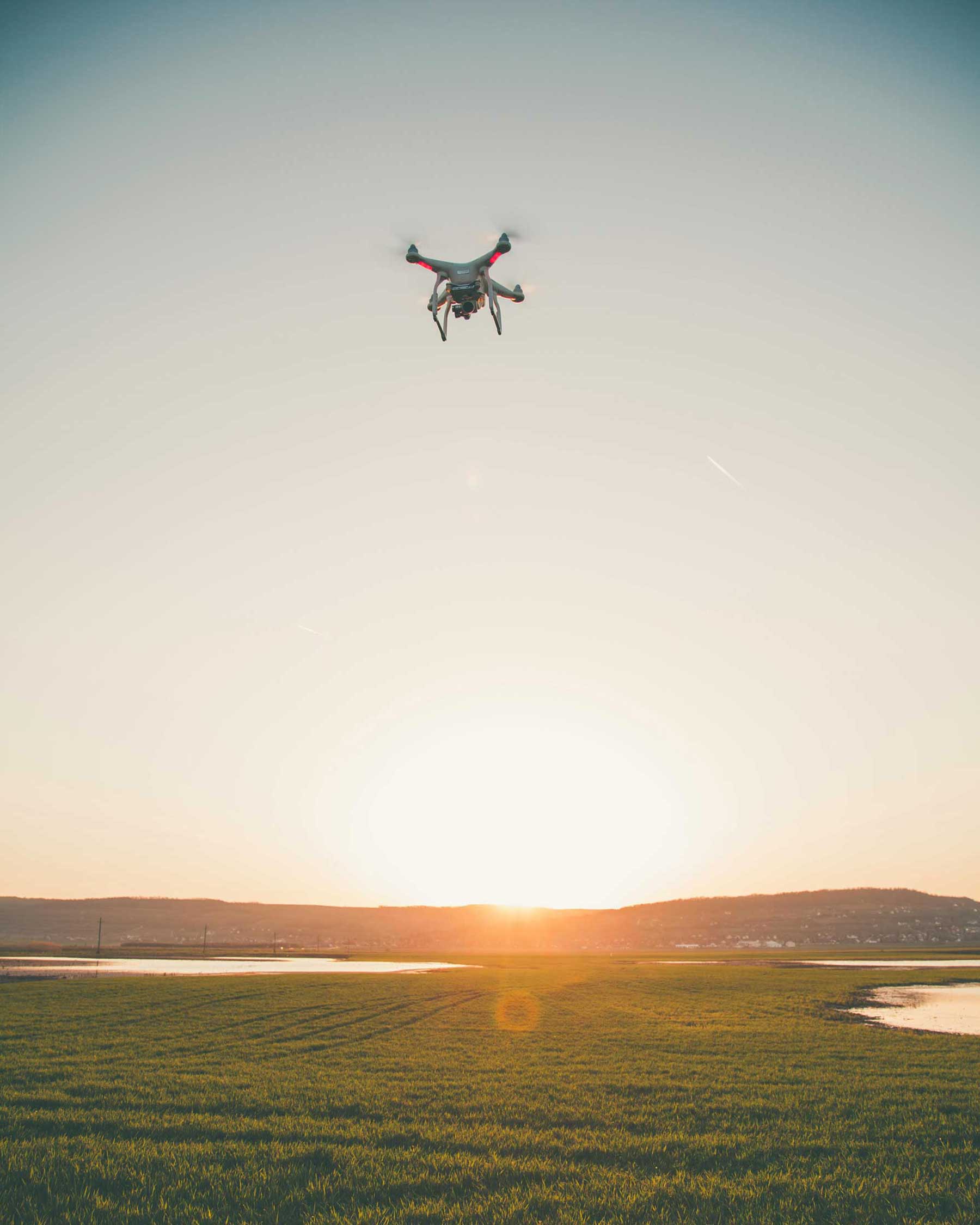 Drone flying over a green field at sunset with hills in the background.