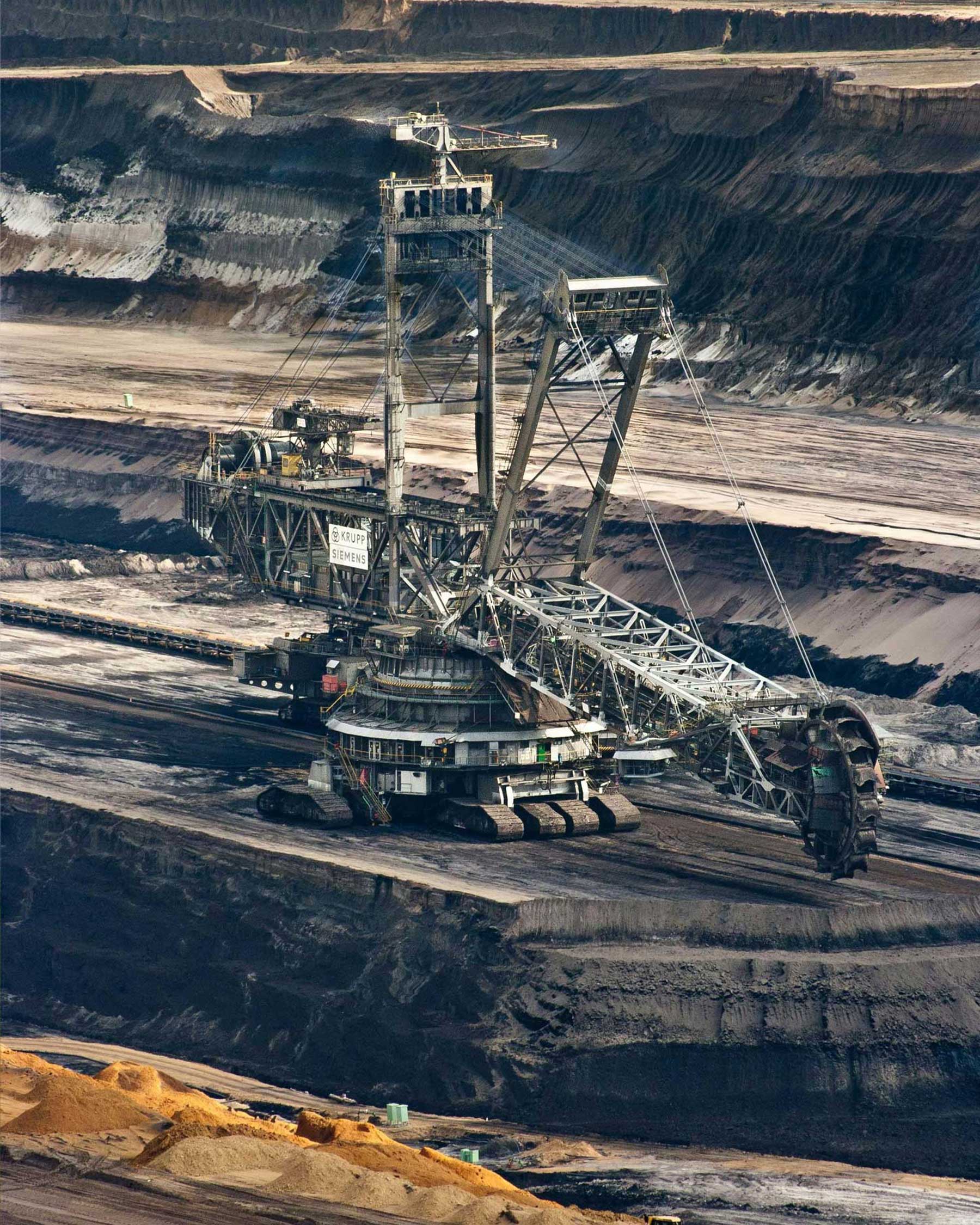 Large bucket-wheel excavator operating in an open-pit mine with terraced soil layers in the background.