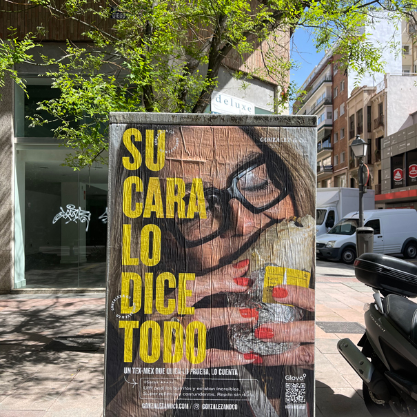 Outdoor advertisement poster showing a woman with glasses and red nail polish holding a wrapped burrito, with large yellow text in Spanish that reads 'Su cara lo dice todo.'