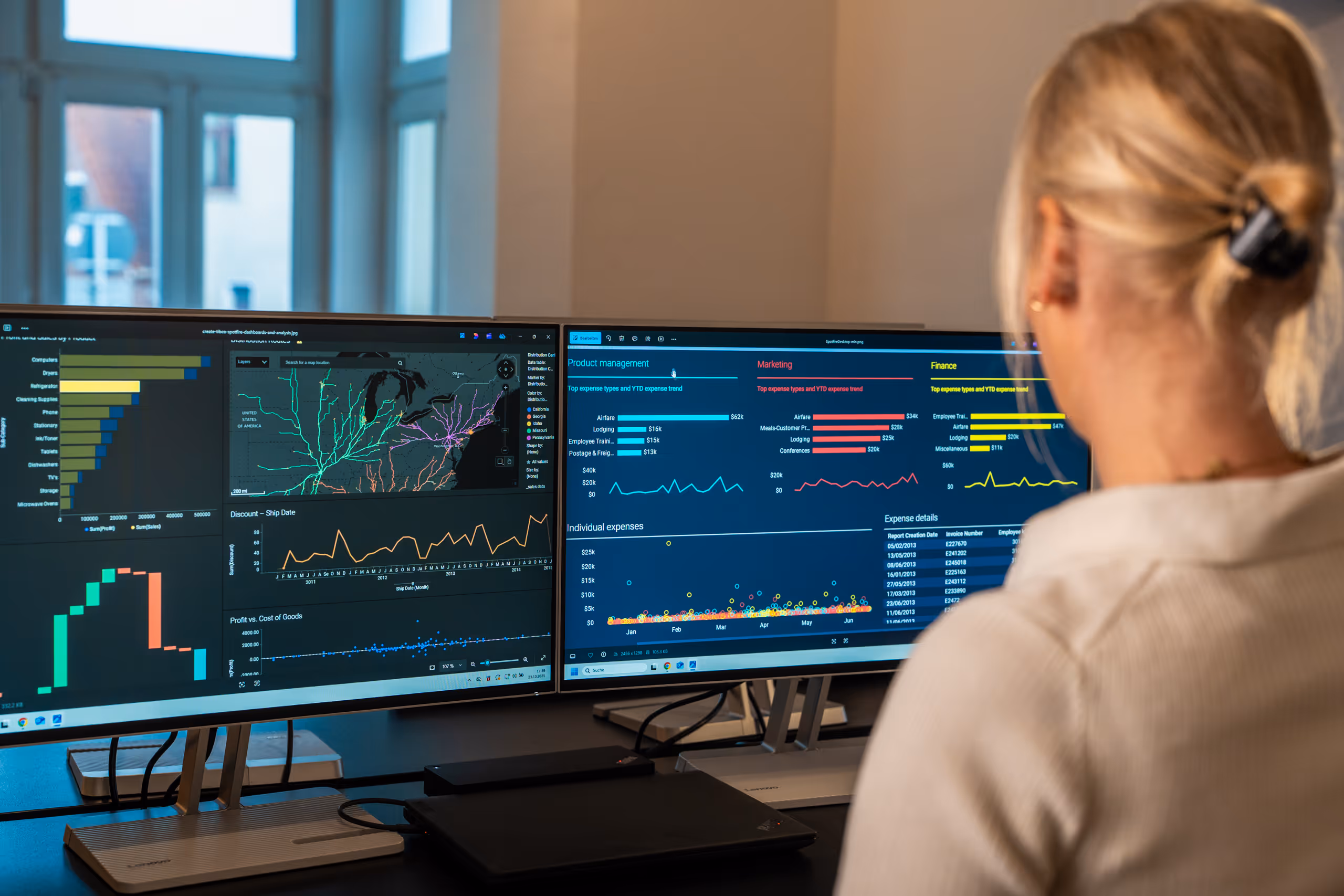Frau mit hellem Haar vor zwei Monitoren, die Datenvisualisierungen und Diagramme anzeigen.