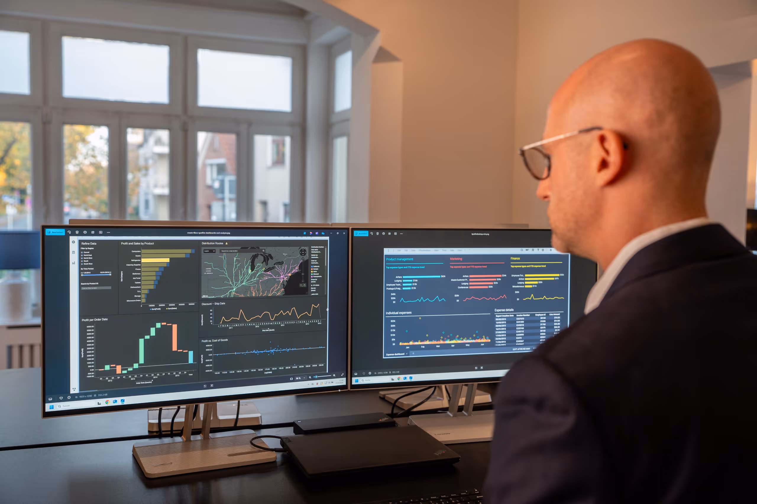 Ein Mann mit Brille, der vor zwei Monitoren sitzt, die Datenvisualisierungen und Graphen anzeigen.