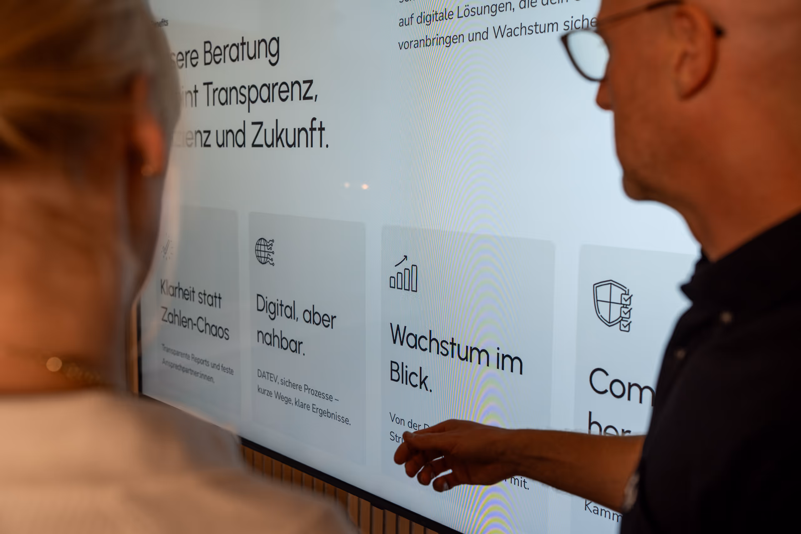 Zwei Personen betrachten einen Bildschirm mit Text und Grafiken zu Beratung, Digitalisierung und Wachstum.
