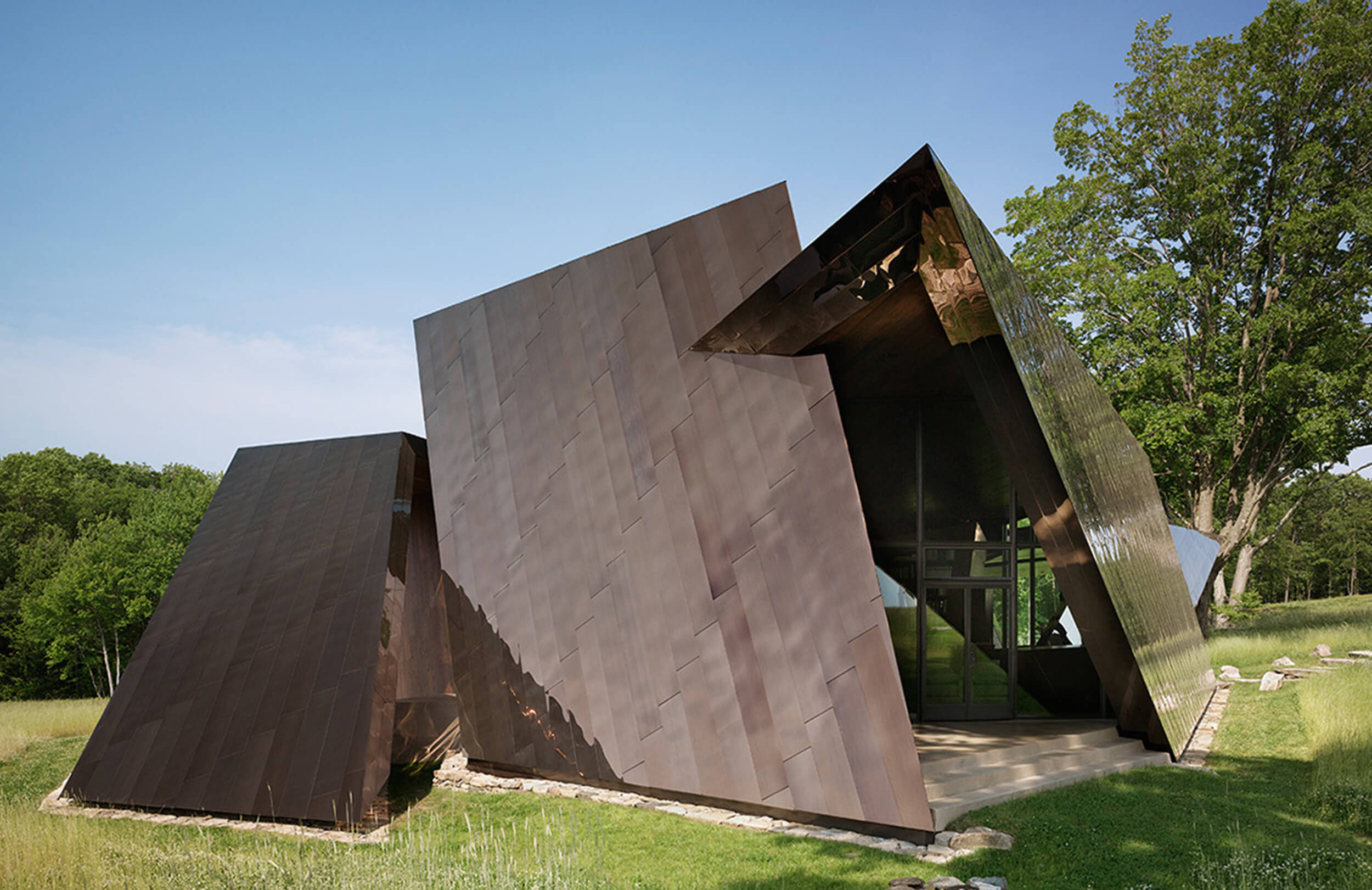 CNR Group luxury home construction: Modern architectural building with large, angular, dark metallic panels surrounded by grass and trees under a clear blue sky.