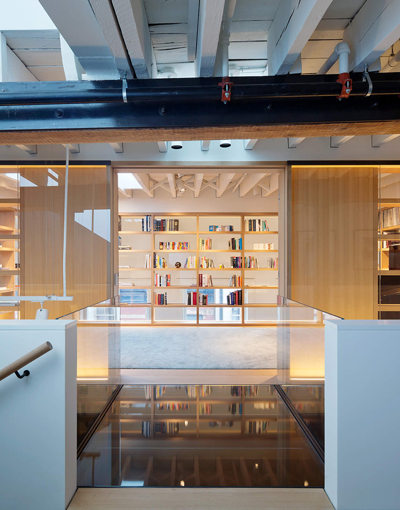 CNR Group luxury home construction project: Modern interior with exposed ceiling beams, glass railing, and a built-in wooden bookshelf filled with books.