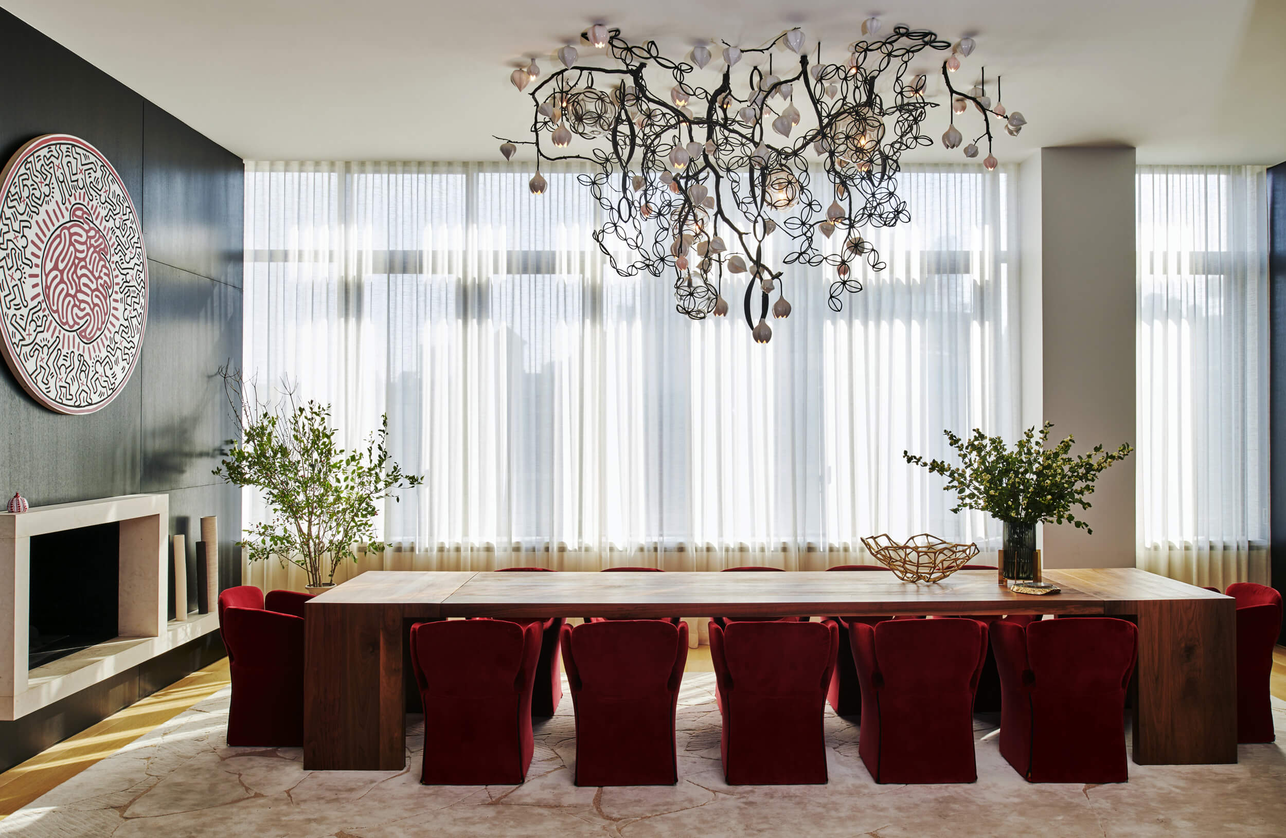 CNR Group luxury home builder project interior: Modern dining room with a long wooden table surrounded by red velvet chairs, large windows with sheer white curtains, and a sculptural chandelier.