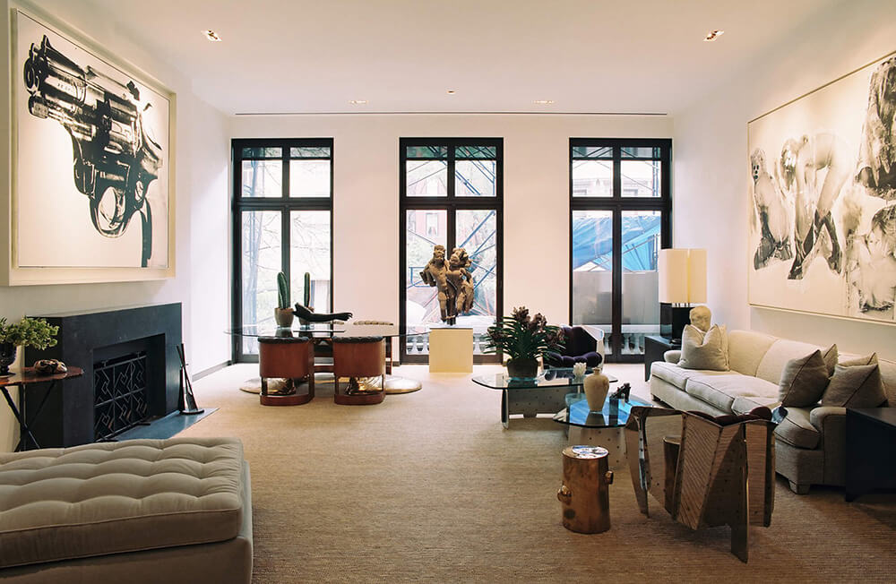 CNR Group NYC luxury home renovation: Modern living room with large windows, sculptures, a beige sofa, glass coffee table, and contemporary art on walls.