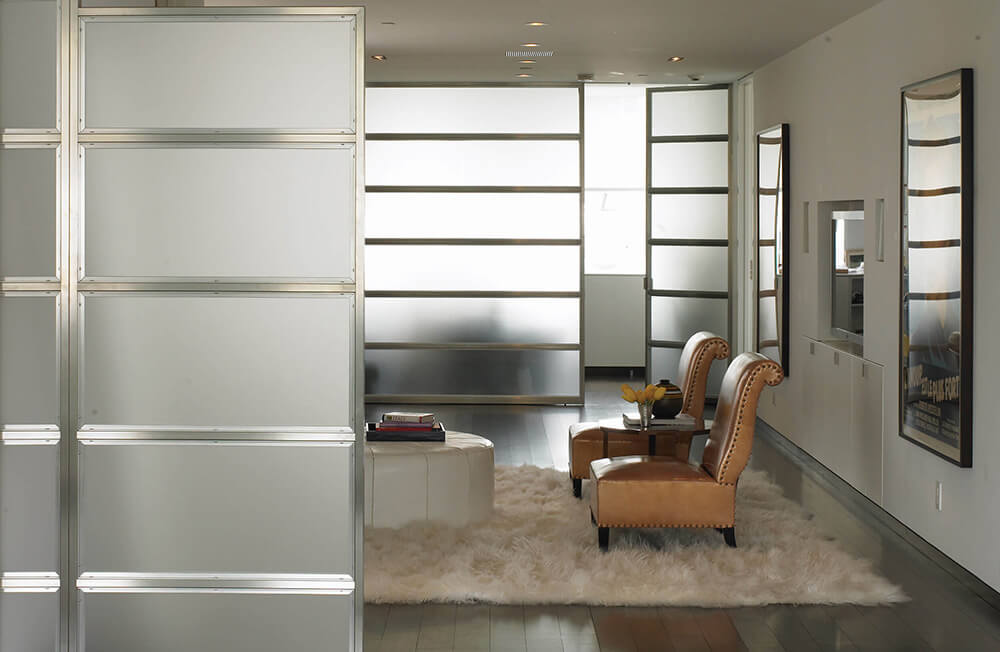 CNR Group NYC luxury home builder project interior: Modern living area with two brown leather armchairs, a small black round table with yellow flowers, a white ottoman, fluffy rug, and frosted glass sliding doors.
