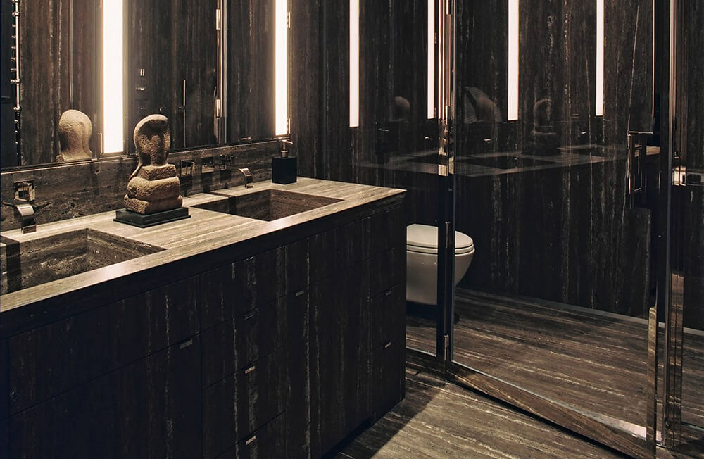 CNR Group luxury home builder project interior: Modern bathroom with dark stone walls and floor, double sinks, and a glass shower door reflecting a toilet.