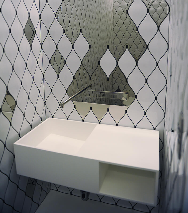 CNR Group NYC luxury home builder project interior: Modern white rectangular bathroom sink mounted on a wall with black and white patterned tile background and a uniquely shaped mirror.