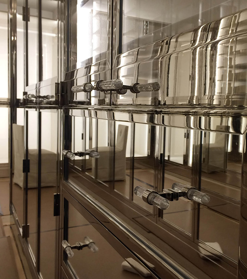 CNR Group NYC luxury home builder project interior: Close-up of shiny mirrored wardrobe drawers with clear crystal handles reflecting a beige chair in the background.