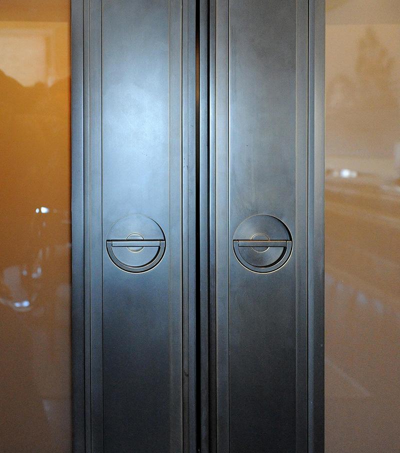 CNR Group NYC luxury home builder project interior: Close-up of modern double metal door with round recessed handles and vertical grooves.