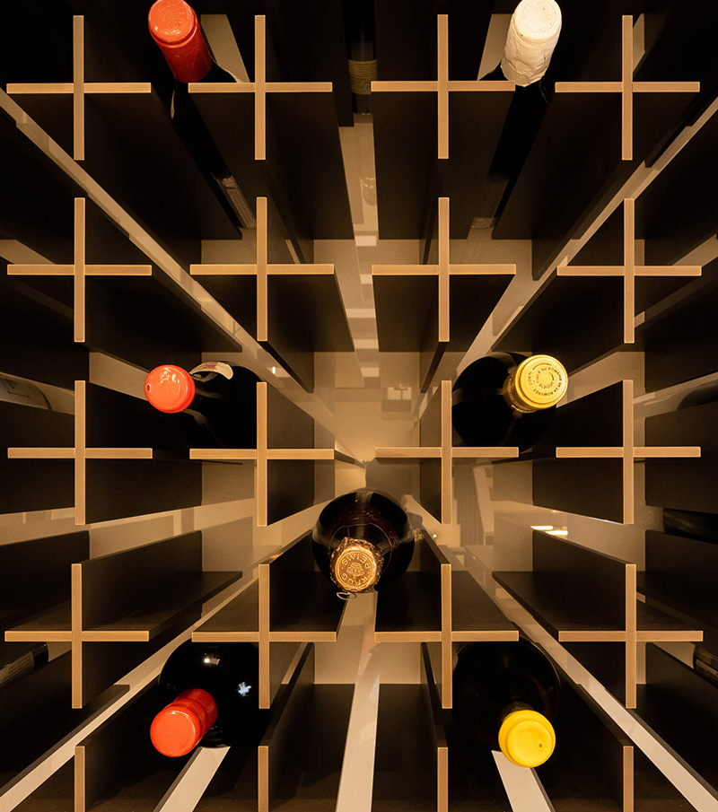 Top-down view of a custom millwork wooden wine rack with several bottles stored horizontally in separate compartments.
