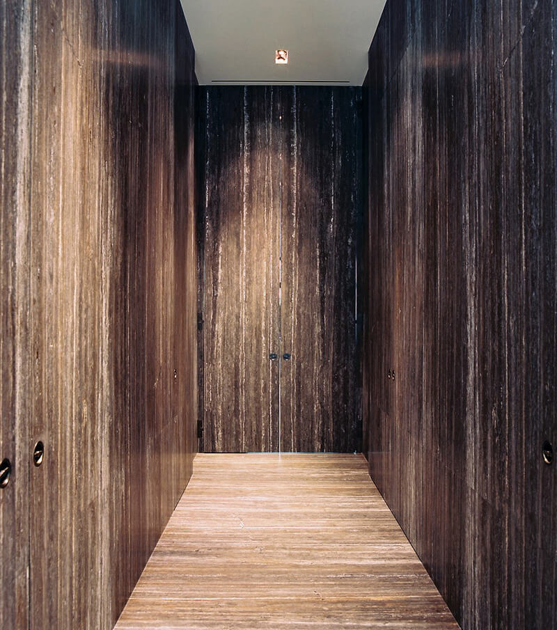 Narrow hallway with dark custom millwork wooden paneled walls and floor leading to a closed double door of the same material.