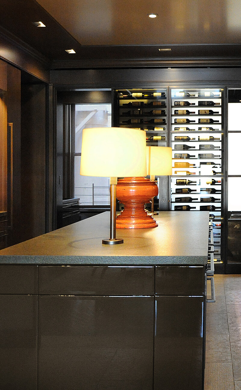 CNR Group NYC luxury home builder project interior: Modern kitchen island with glowing table lamps and a wine rack filled with bottles in the background.