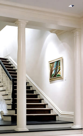 CNR Group NYC luxury home builder: Interior staircase with dark wooden steps, white risers, two white columns, and an abstract painting on the wall.