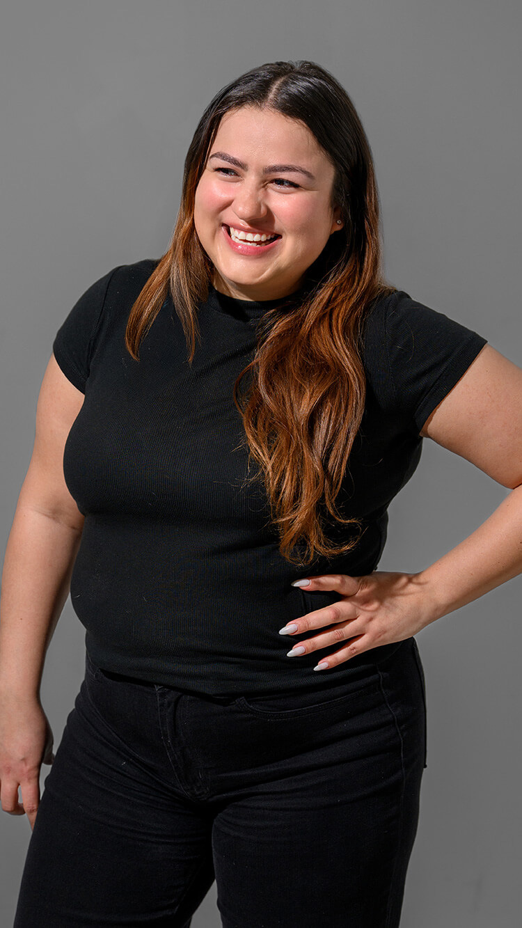CNR Group luxury builders team member: Michelle. Smiling woman with long brown hair wearing a black t-shirt and black pants, standing against a gray background.