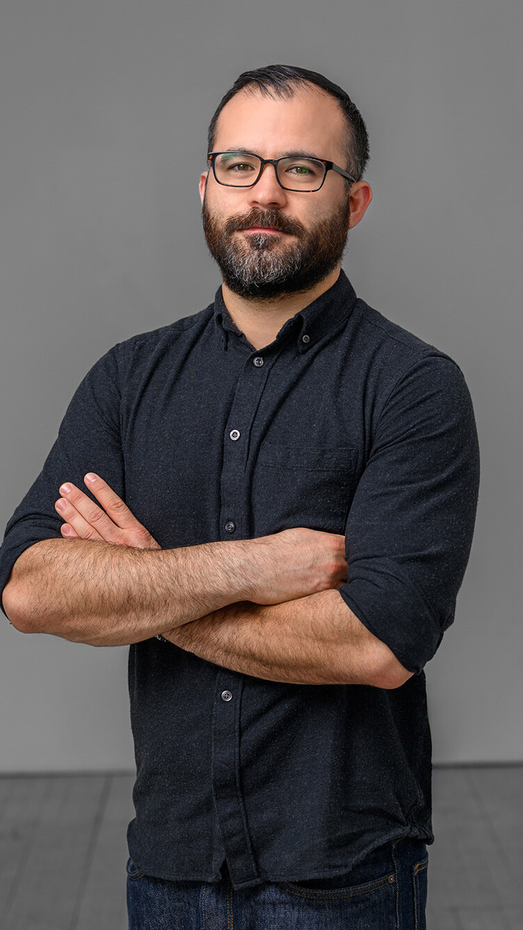 CNR Group luxury builders team member: Garry. Bearded man wearing glasses and a dark button-up shirt with sleeves rolled up, standing with arms crossed against a plain gray background.