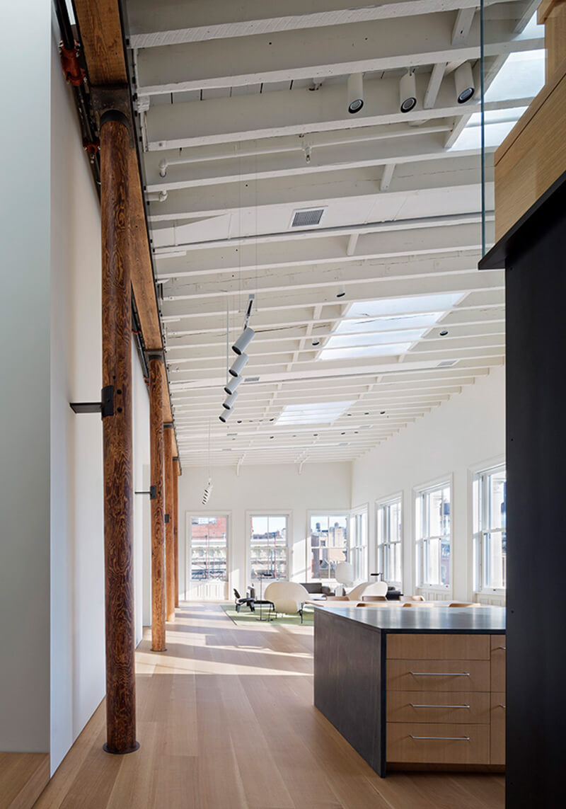 CNR Group NYC luxury builders: Bright open loft space with wooden floors, custom millwork exposed wooden columns, white beams on ceiling, and modern seating area near large windows.