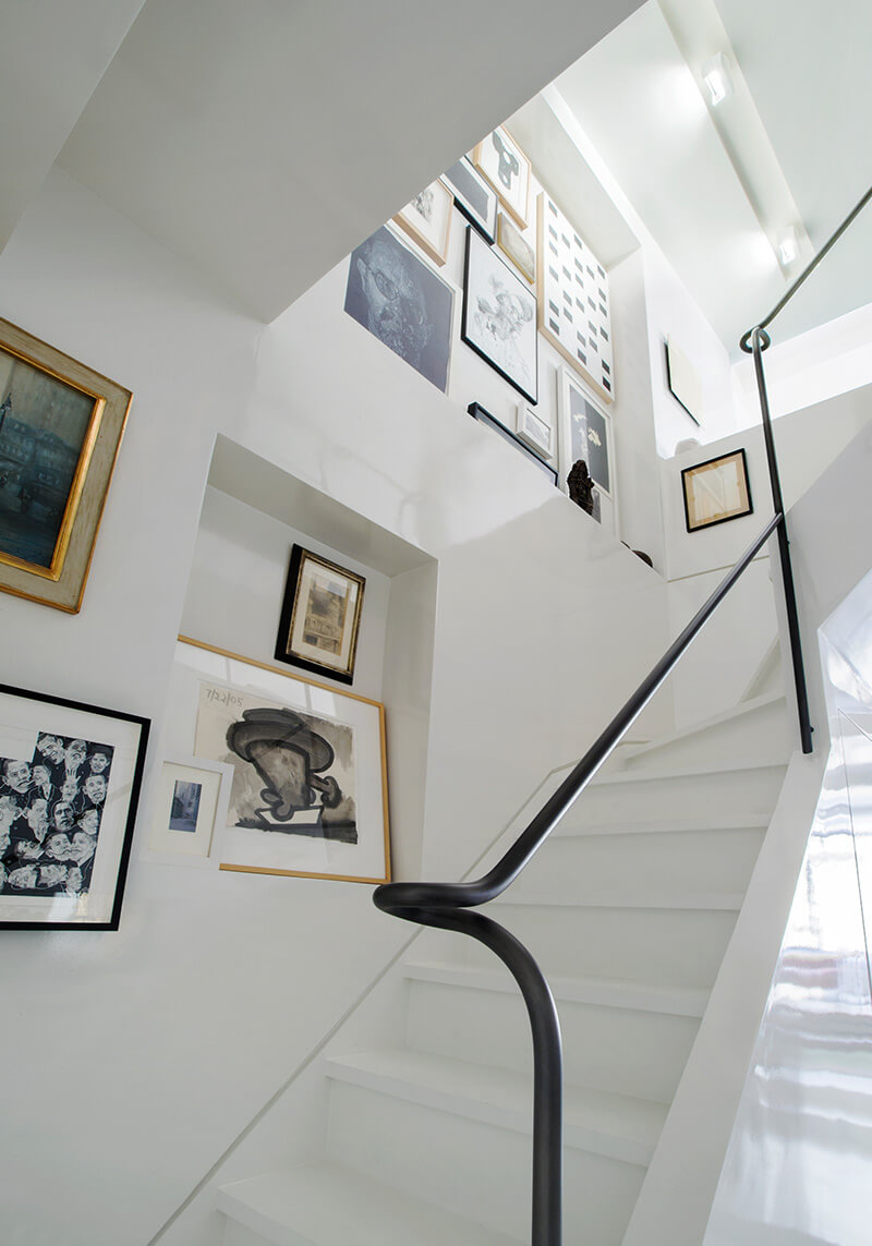 White staircase with black metalwork handrail and walls decorated with framed abstract and portrait artworks.