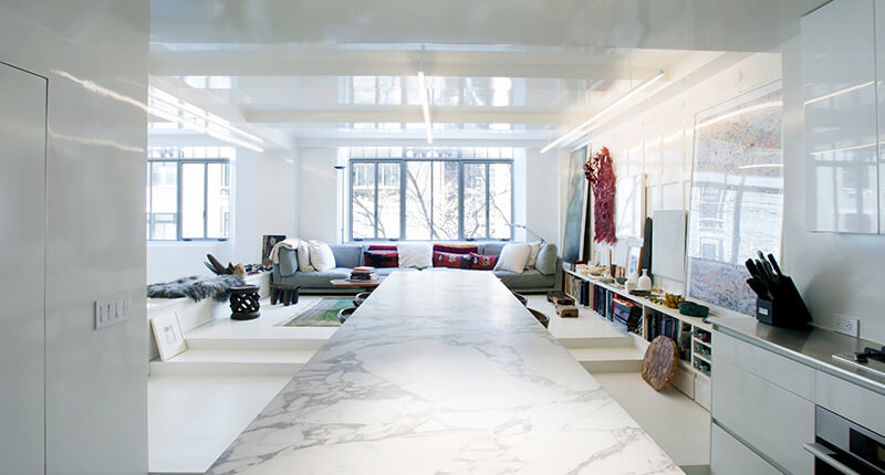 CNR Group NYC luxury home builders: Modern bright living room with large marble table, gray sectional sofa, large windows, and built-in shelving with art pieces.