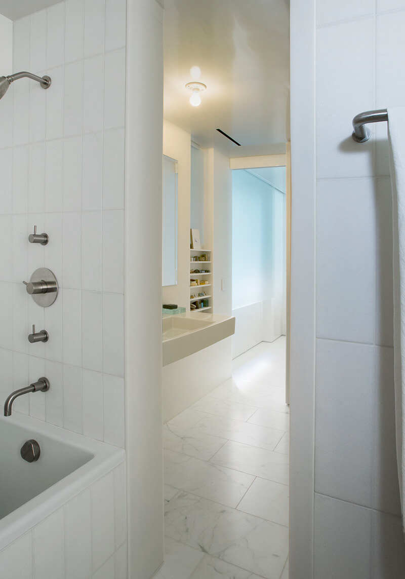 CNR Group NYC luxury home project management: Bright modern bathroom featuring a white tile bathtub with silver fixtures, a floating sink, and marble floor tiles.
