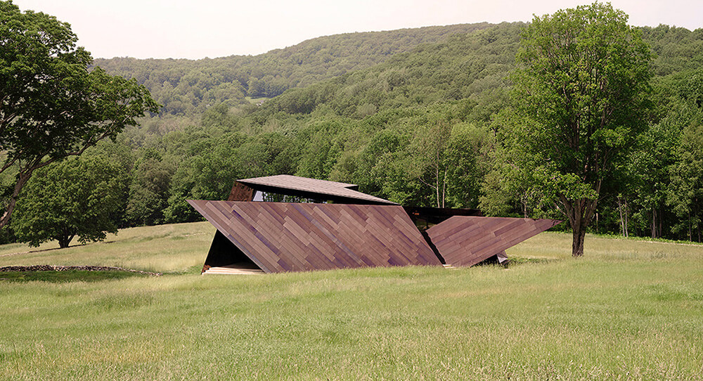 CNR Group luxury home construction: Modern architectural structure with angular panels situated in a grassy field surrounded by trees and hills.
