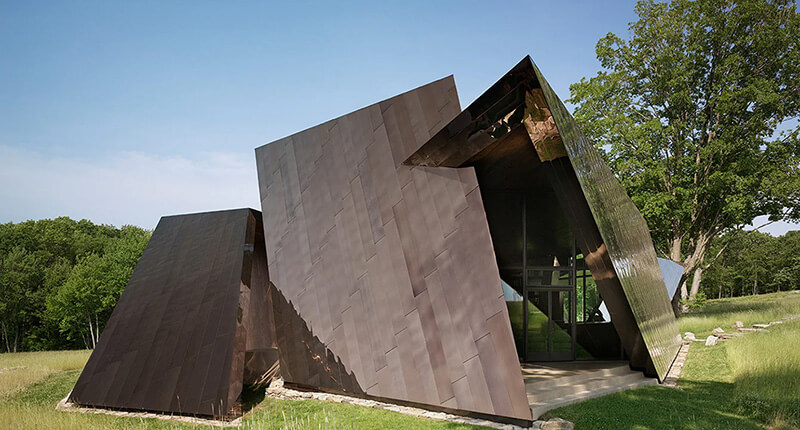 CNR Group luxury home project management: Modern angular house situated in a grassy field with trees in the background under a clear blue sky.