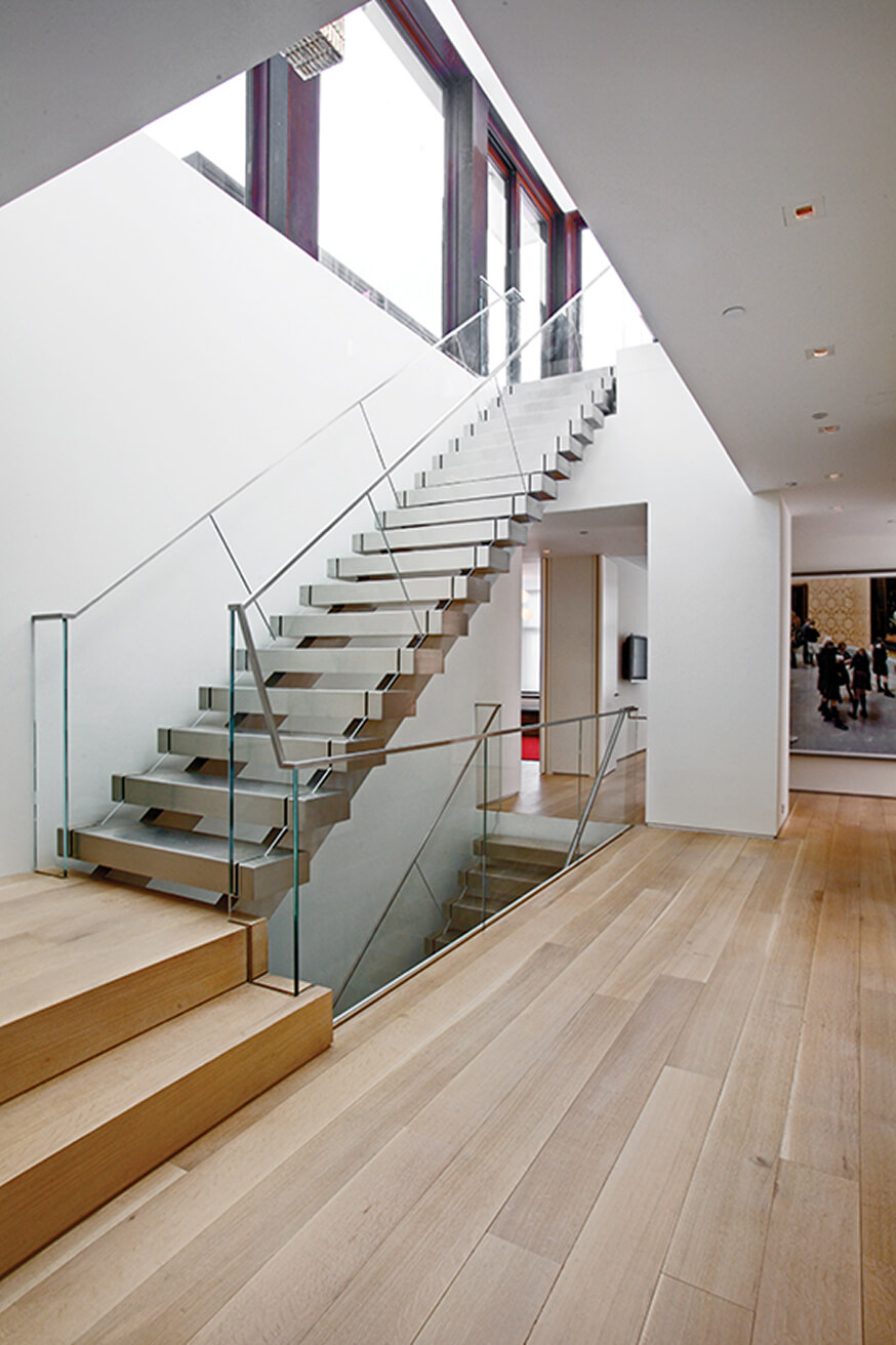 Modern interior with a floating metalwork staircase featuring glass railings and light wood flooring.